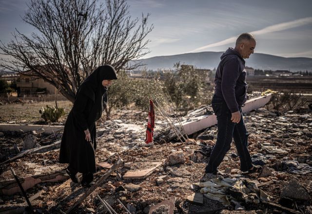 Ruba and Hassan Chamas walk through the ruins of their bombed home; she mourns her son lost in the strike."