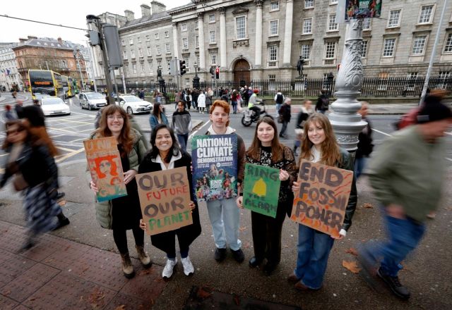 Students stand outside Trinity College Dublin holding signs calling for climate action.