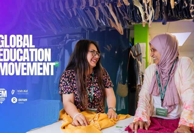 Two women speaking to each other while holding clothes on a table