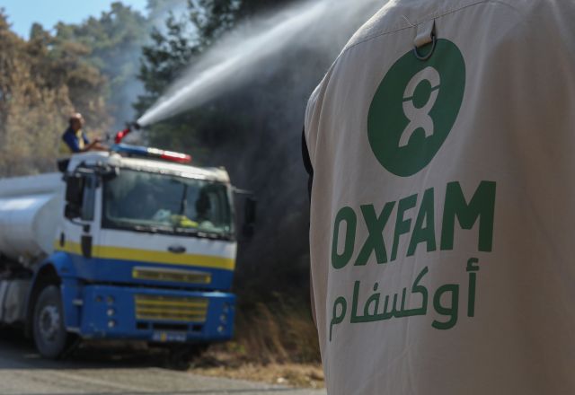 An Oxfam staff member stands near Civil Defense vehicles as volunteers battle wildfires in Qastal Ma'af, rural Latakia.