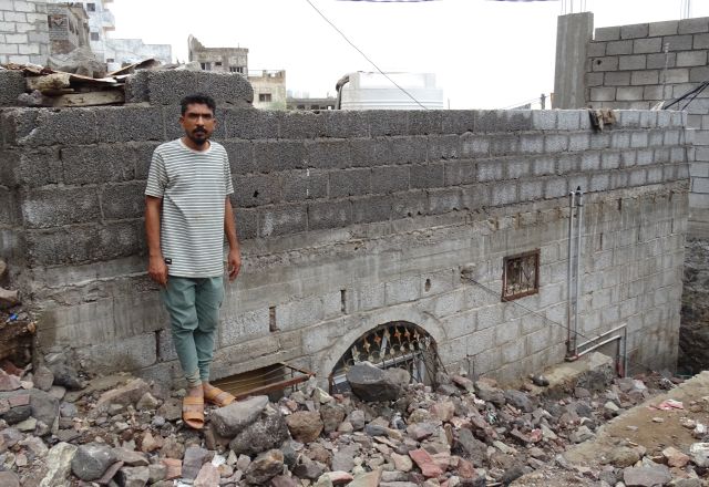 Issa standing next to his home buried under rubble.