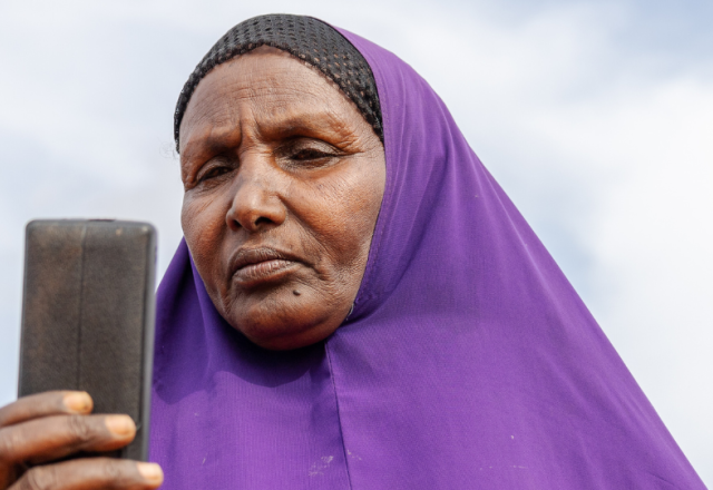 Ebla Hussein Ahmed reading a message from her mobile phone at her home in Elben, Wajir County, Kenya. She receives her monthly cash payment notification via her phone.