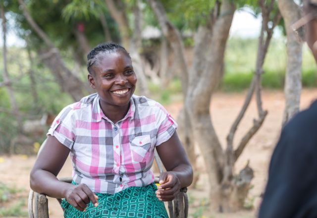 Angela Chiyala is a farmer. She is sitting and smiling in her farm in Zambia