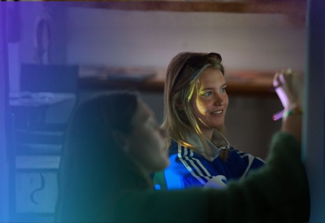 Two young girls working together at a board, with one person writing while the other observes in a softly lit room.