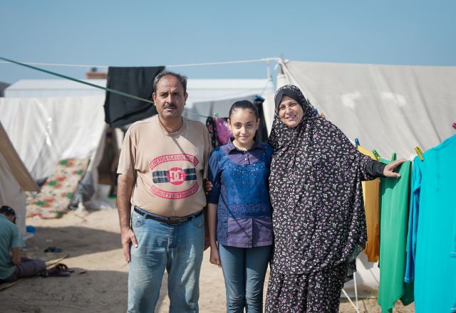 Sawsan*, her husband and one of her daughters are standing in front of their new tent in the newly established Tents camp established in Khan Younis by the UNRWA