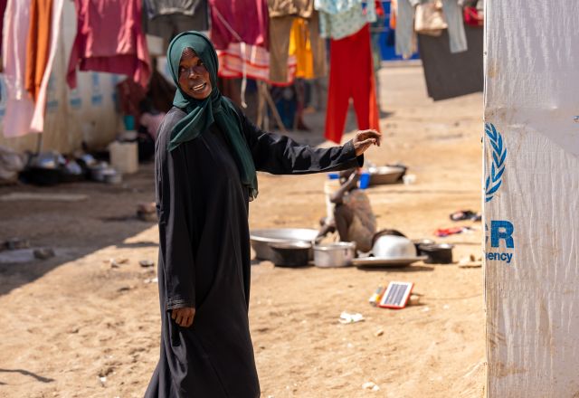 Woman wearing black standing on dry sand in a refugee camp.