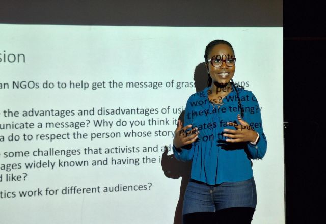 Female speaker in front of a projection of a presentation