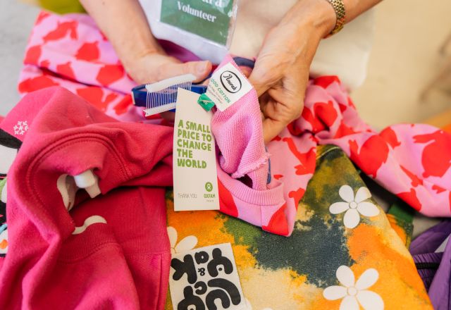 Pieces of clothing laying down in a table and a volunteer hands labelling the items