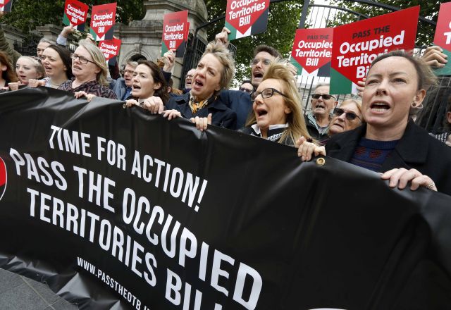 Protest group outside a government building holding a banner and signs calling to pass the Occupied Territories Bill.