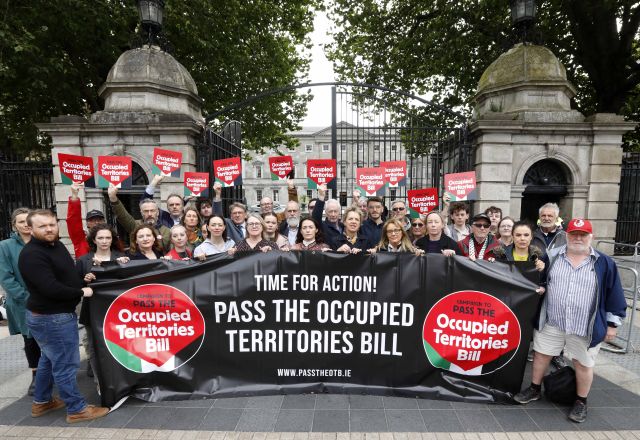 Protest group outside a government building holding a banner and signs calling to pass the Occupied Territories Bill.