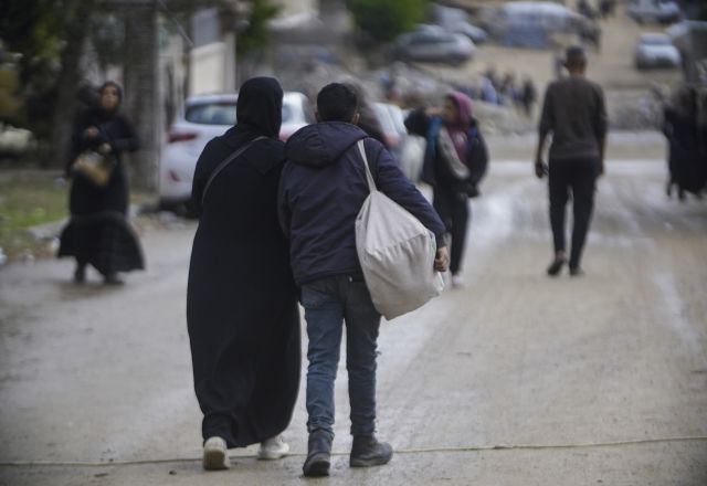 Man and woman carrying heavy load walk down road in Occupied Palestine.