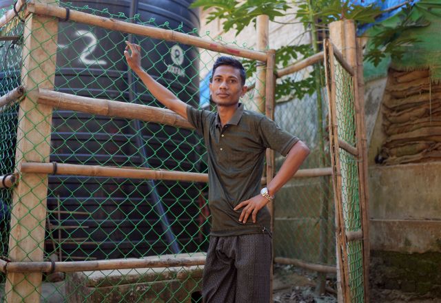 Young man standing in front of water tank in Bangladesh.