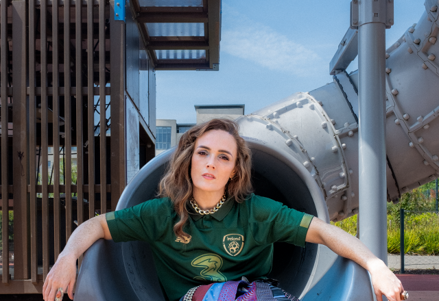 Emma Doran is wearing an Ireland football jersey and sitting on a grey playground slide.