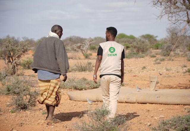 Oxfam staff member and Somalian community member walk through dry land.