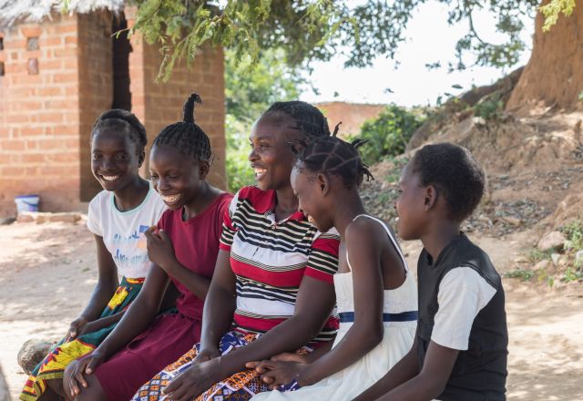 A woman and five girls sit in a row outside; they are laughing
