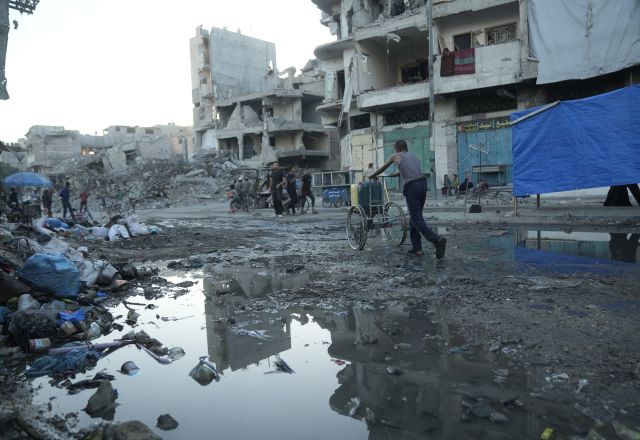 Destroyed buildings in Gaza. A man is pushing a cart with jerry cans on the top among the rubble