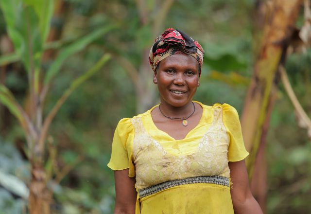 A lady in a yellow dress smiles at the camera. There are trees in the background