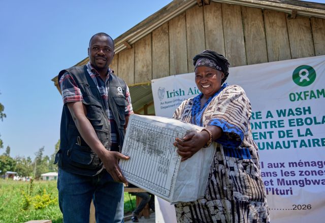 Two people stand holding a large box which is a non-food item kit