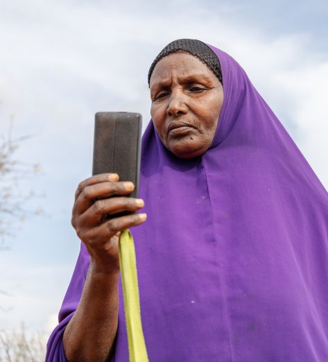 Ebla Hussein Ahmed reading a message from her mobile phone at her home in Elben, Wajir County, Kenya. She receives her monthly cash payment notification via her phone.