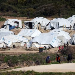 Asylum seekers stand next to tents near the sea at the Mavrovouni camp on Lesbos