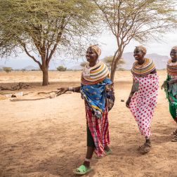 Five ladies in traditional attire walk across a dry, open landscape in Ongeli Village, Marsabit, heading to a participatory training under the DFAT-funded CLTS project by SND.