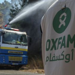An Oxfam staff member stands near Civil Defense vehicles as volunteers battle wildfires in Qastal Ma'af, rural Latakia.