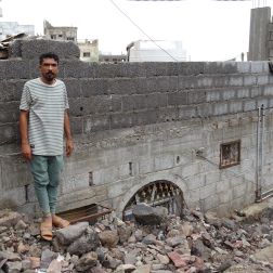 Issa standing next to his home buried under rubble.