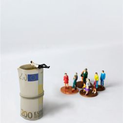 Miniature character setup with man in suit relaxing on top of a pile of 200 euro bills and a group of ordinary people standing on cents