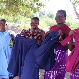 Four women from the The Chisomo Tailoring Club holding skirts and dresses they have made as part of the club.
