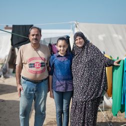 Sawsan*, her husband and one of her daughters are standing in front of their new tent in the newly established Tents camp established in Khan Younis by the UNRWA