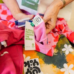 Pieces of clothing laying down in a table and a volunteer hands labelling the items