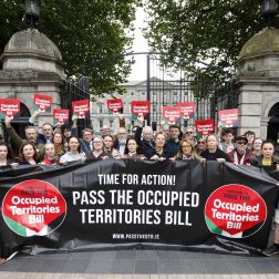 Protest group outside a government building holding a banner and signs calling to pass the Occupied Territories Bill.