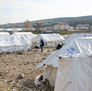 Asylum seekers stand next to tents near the sea at the Mavrovouni camp on Lesbos