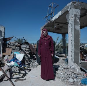 A woman wearing a red hijab stands among the rubble of a destroyed home. She is showing signs of pregnancy in Gaza.
