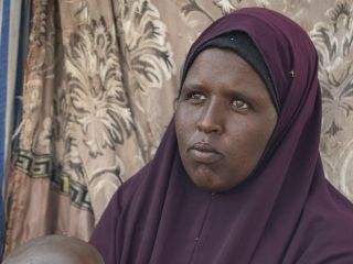 Layla Abdi Eige with her youngest child in front of her hut; she is living in Cal Ciidle, a camp for internally displaced persons (IDPs).